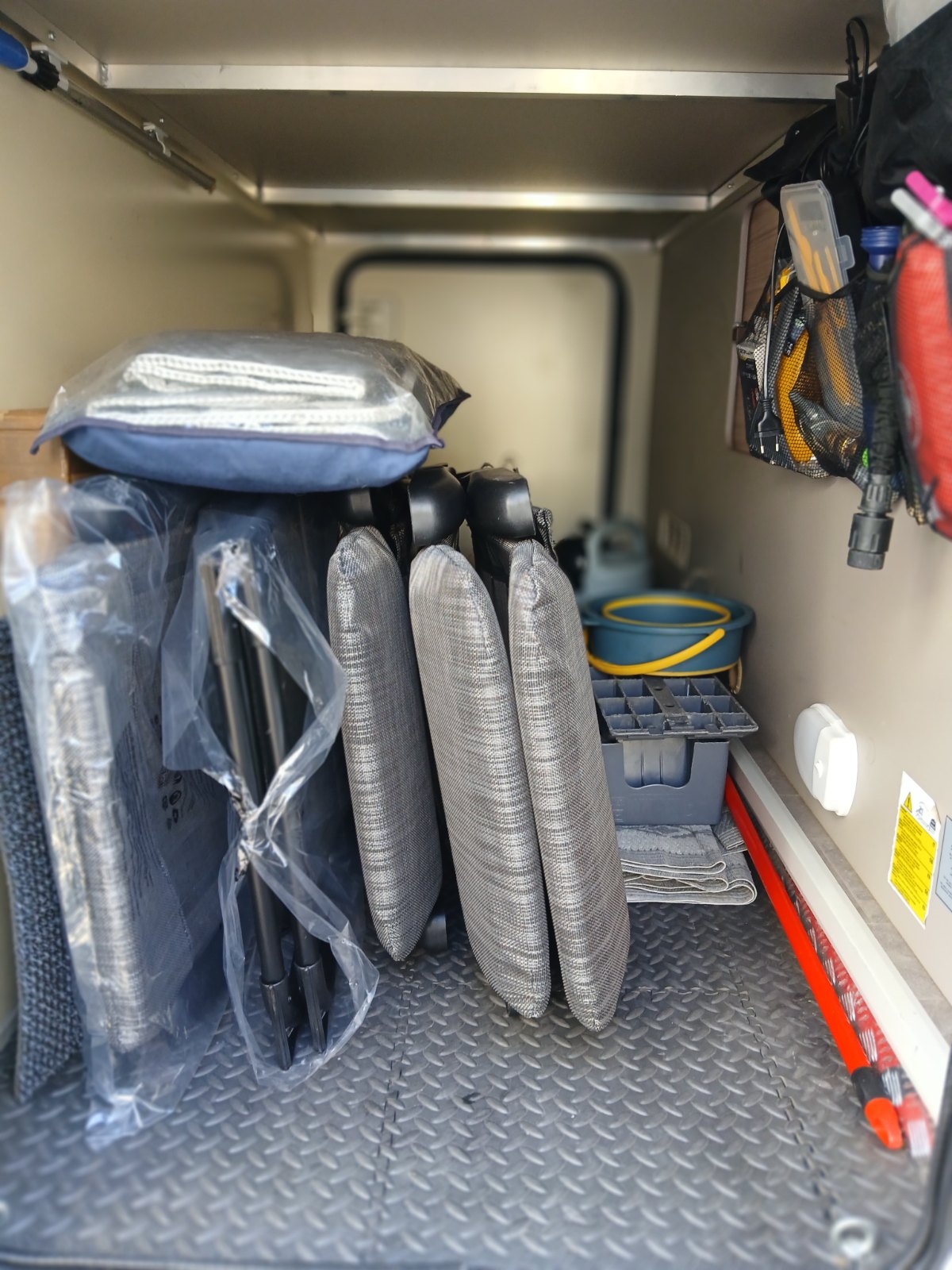 Geöffnete Heckgarage mit verpackten Campingstühlen, Campingzubehör und einer Netztasche mit Kabeln und Werkzeug