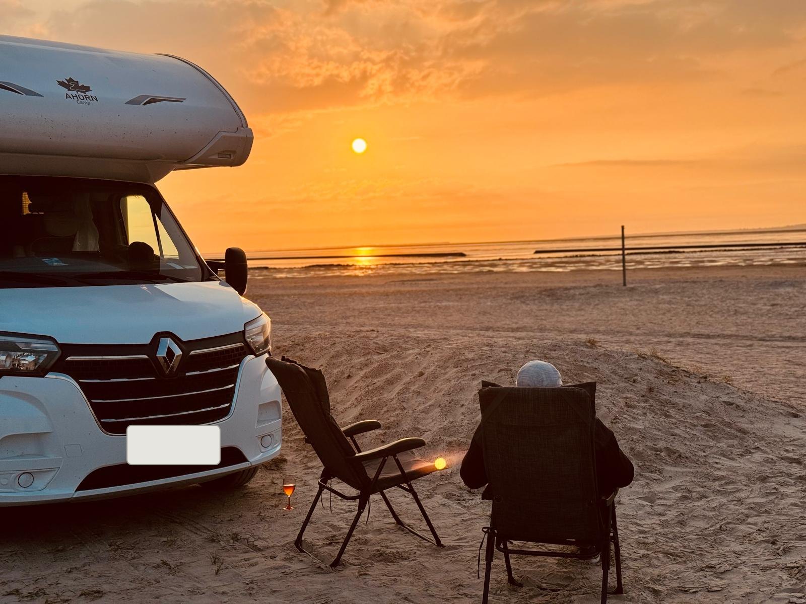 Wohnmobil am Strand bei Sonnenuntergang, davor Campingstühle